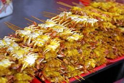 Small dried crab kebabs are piled up on trays. 